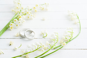 Lily of the valley with wedding rings on white wooden