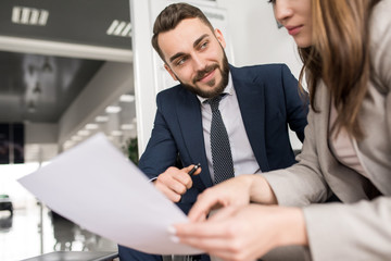 Wall Mural - Portrait of two modern business people discussing documents in office, focus on handsome man smiling and looking at woman