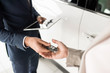 © Seventyfour - High angle close up of car salesman giving keys to client standing next to white luxury car, copy space