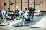 Young and beautiful couple training with exercise rowing machines in the gym