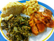 Southern comfort food in America. Close up serving of kale greens, candied yams, macaroni and cheese, and cornbread served on a white and blue plate.