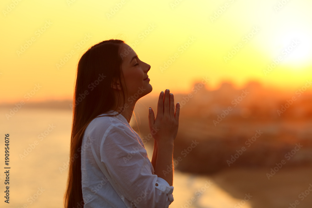 Profile of a woman praying at sunset - obrazy, fototapety, plakaty 