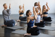 Group of young sporty people practicing yoga lesson with instructor, sitting in Cow Face exercise, Gomukasana pose, working out, indoor full length, students training in club, studio