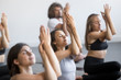 © fizkes - Group of young sporty people practicing yoga lesson with instructor, sitting in Cow Face exercise, Gomukasana pose, working out, indoor close up of hands, students training in club, studio