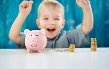 Two Years Old Child Sitting On The Floor And Putting A Coin Into A Piggybank