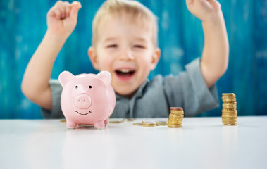 two years old child sitting on the floor and putting a coin into a piggybank