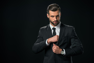 handsome businessman taking something from pocket of jacket, isolated on black