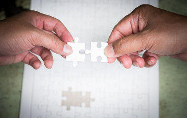 two hands try to put the last piece of jigsaw puzzle to complete the mission