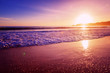 Beautiful bright purple purple sunset on the ocean, sandy beach, waves and glare of the sun