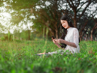 Sticker - woman with headphones listening to music from smart phone and sitting in park