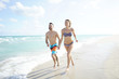 © goodluz - Young couple on vacation running on a sandy beach