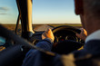 Close up of senior driver hands holding steering wheel and driving on the road at sunset.