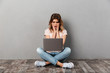 © Drobot Dean - Surprised woman in t-shirt sitting on floor with laptop computer