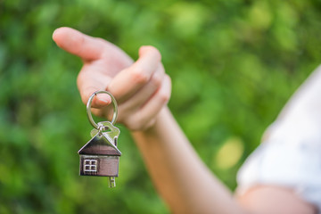 house key in woman hand and green leaves background