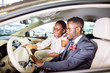 Happy beautiful african couple is choosing new car at dealership.