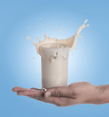 Sticker - Hand holding glass of milk with a splash on a blue background