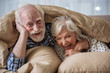 Leinwandbild Motiv Cheerful old married couple lying in bed under blanket. Woman is laughing and man is looking at camera with smile. Concept of happiness