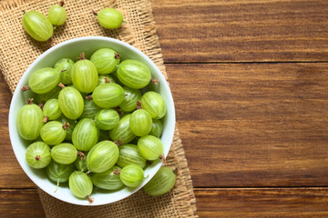 Poster - Raw gooseberries (lat. Ribes uva-crispa) in bowl, photographed overhead on dark wood with natural light (Selective Focus, Focus on the gooseberries on the top)