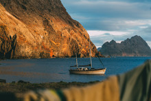 View On A White Sailing Boat Anchored In Natural Harbour In A Secret Bay Close To Desertas Islands During Sunset With Orange Sunny Mountains In The Background And Wet Clothes Hanged In Foreground 
