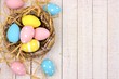 Springtime nest with pink, yellow and blue painted Easter Eggs. Side border against a rustic white wood background.
