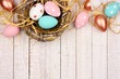 Springtime nest with pink, rose gold and turquoise painted Easter Eggs. Top border against a rustic white wood background.