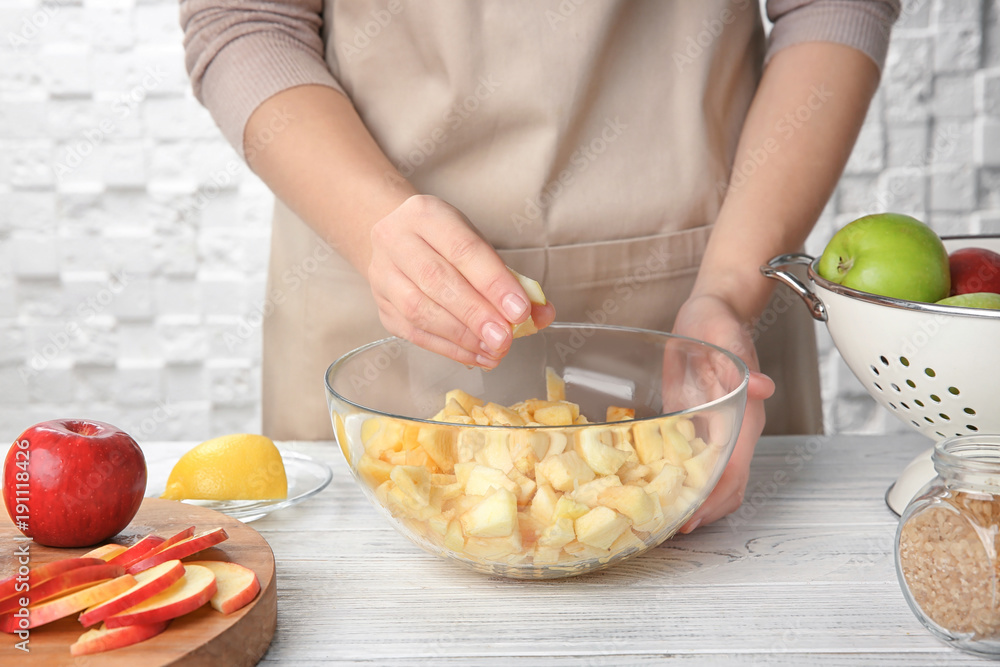 Woman putting cut apples in glass bowl on kitchen table