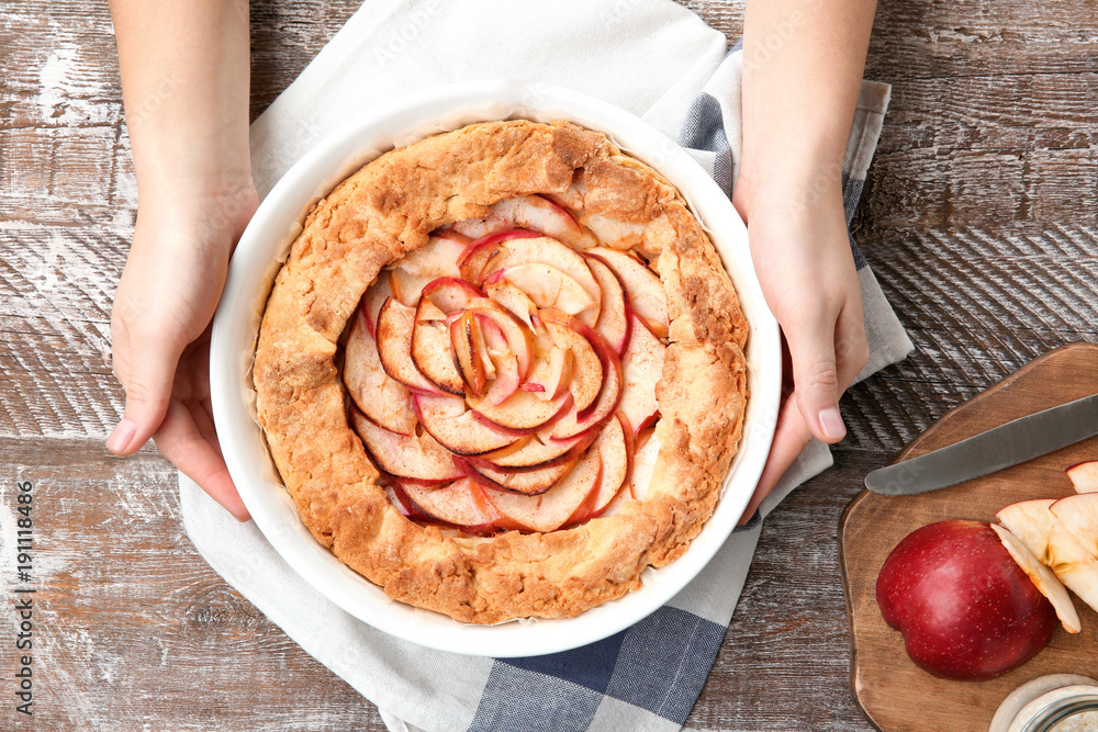 Female hands with freshly cooked apple tart on wooden background