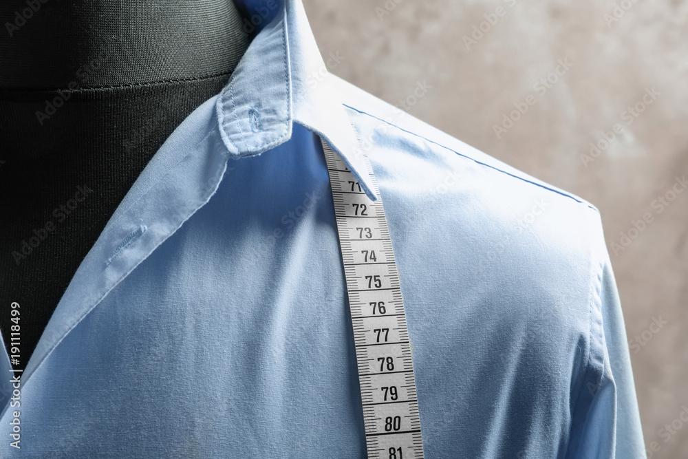 Shirt with measuring tape on tailor mannequin against light background