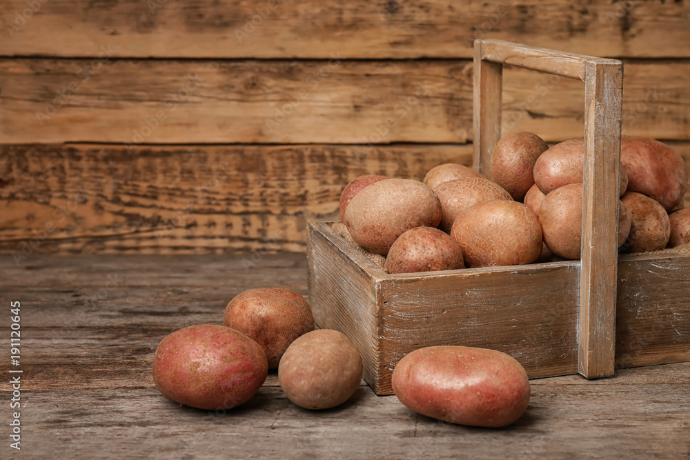 Wooden basket with fresh raw potatoes on table