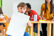 © weedezign - Kid boy holding blank white poster with diversity friends and teacher at background,Kindergarten school,mock up chalkboard for adding text