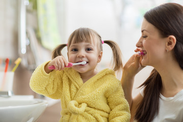 Beautiful mother and kid brushing teeth in bathroom