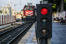 Traffic Light Shows Red Signal On Railway; Railway Station And The Train Is Coming