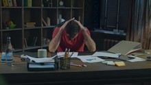 Tired business man at cozy office. Young businessman tired at evening work. Depressed man putting hands on head at desk. Disappointed man at table in home office. Stress work concept