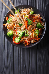 fried soba noodles with mushrooms, broccoli, carrots, peppers closeup on a plate. Vertical top view