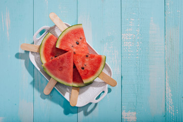 Slices of watermelon on plate on blue wooden desk.