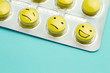 Yellow pills and funny faces in a blister on a blue background. The concept of antidepressants and healing