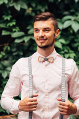 Wall Mural - guy with wooden bow tie and suspenders smiles against the background of green leaves