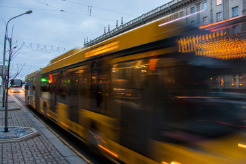 The motion of a blurred bus on the avenue at dusk.