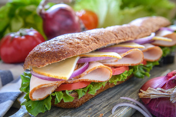 Sub sandwich with turkey, cheese, onions and tomato in a roll on a cutting board