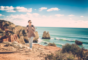 A traveler with a backpack walks along the rocky coast of the ocean, admiring the incredible scenery. Portugal, the Algarve, a popular destination for travel in Europe