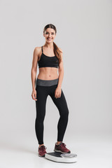 full-length image of female sport trainer measuring her weight after fitness standing on scale, isol