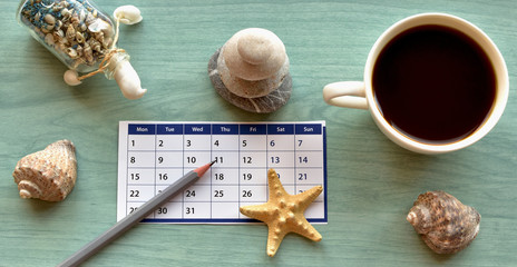 early booking dreams and plans: a cup of coffee, calendar sheet, pencil, dried starfish, a souvenir from the seaside resort of the bottle with blue sand and seashells pyramid of stones, seashells