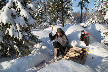 Campfire in deep snow, preparation, man split firewood with a knife