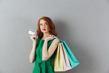 Poster - Thoughtful redhead young woman holding shopping bags