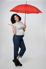 Pregnant Woman Standing In Full Length Under Red Umbrella Smiling Looking At Camera Pointing At Blank Copy Space