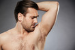 Close up portrait of a shirtless man smelling his armpit