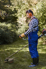 Wall Mural - Busy man using a weedwacker at garden