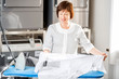 Senior washwoman ironing white shirt with professional iron in the laundry