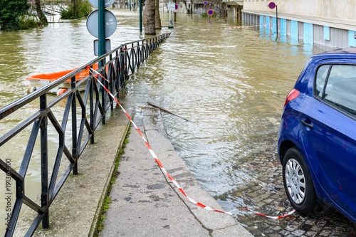 Plakat Podczas zimowego powodzi Sekwany w Paryżu, w styczniu 2018 roku, poziom wody powodziowej dociera do tylnych kół samochodu zaparkowanego w małej pochyłej ulicy prowadzącej w dół do rzeki.