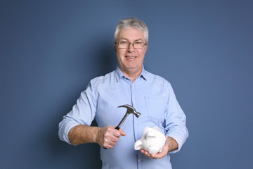 Poster - Mature man holding hammer over piggy bank on color background